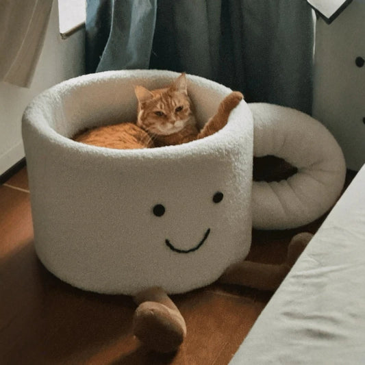 Orange tabby cat resting comfortably inside a plush white coffee mug-shaped cute cat bed.